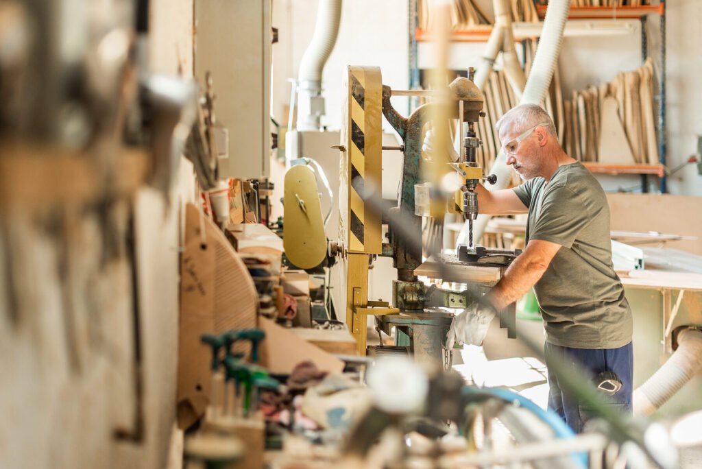 Älterer Facharbeiter bohrt in einer Werkstatt an einer Säulenbohrmaschine älterer Bauart ohne digitale Steuerung